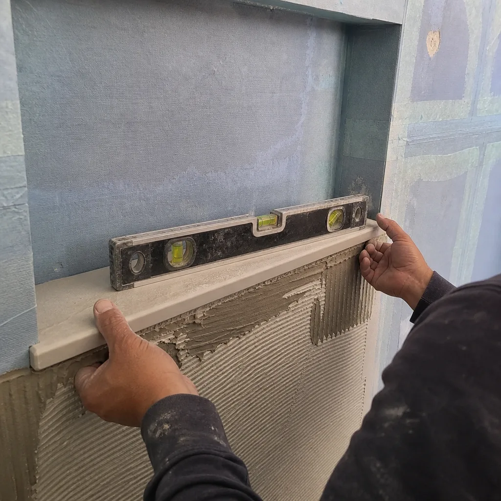 Contractor using a level to install a stone shelf in shower